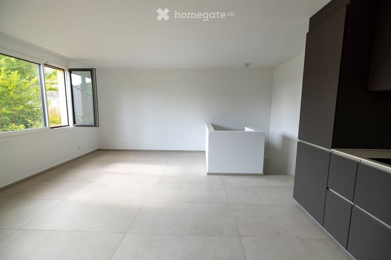 Empty room with tiled floor, white walls, large windows, and dark grey cabinets.