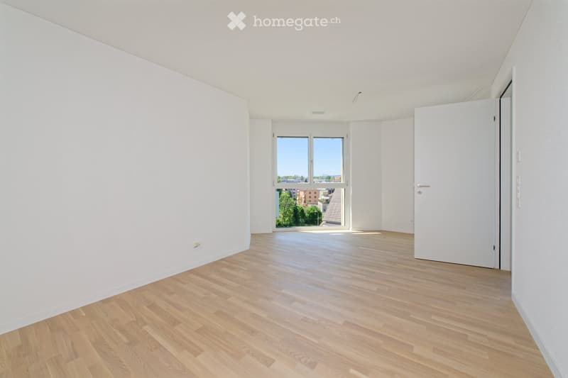 Empty room with white walls, wooden flooring, and large windows offering a view of the outside. No furniture or equipment is present.