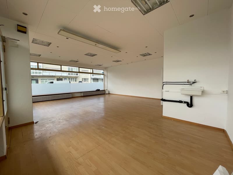 Empty room with wooden flooring, white walls, and a sink in the corner. Large windows provide natural light.