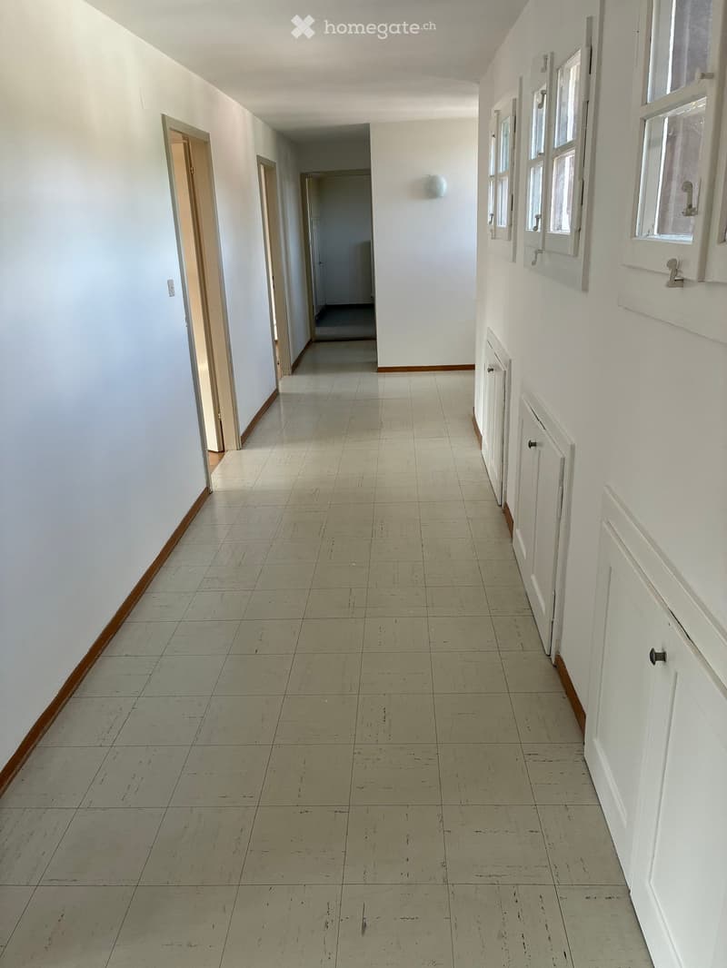 Empty hallway with white walls, tiled floor, and several doors leading to other rooms.