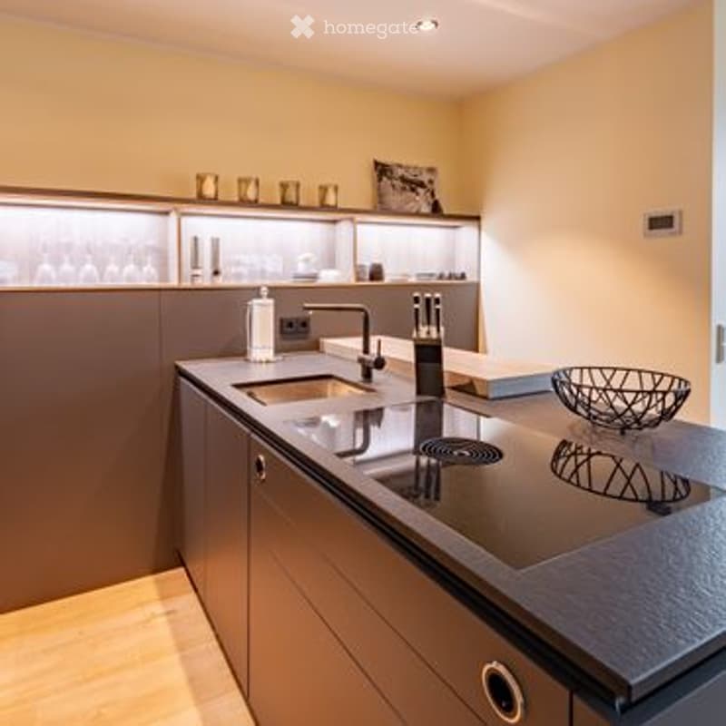 Modern kitchen with a dark countertop, stainless steel sink, and built-in appliances. The space features sleek cabinetry and a minimalist design.