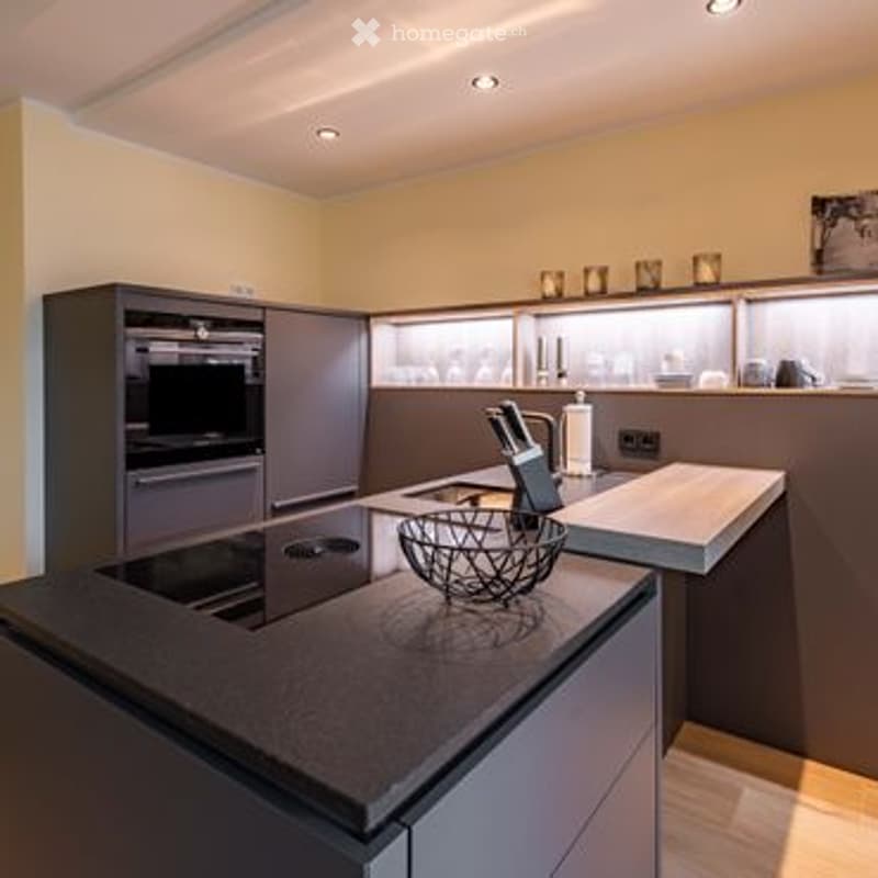 Modern kitchen with grey cabinets, induction cooktop, built-in oven, and a central island with a bowl and decorative candles.