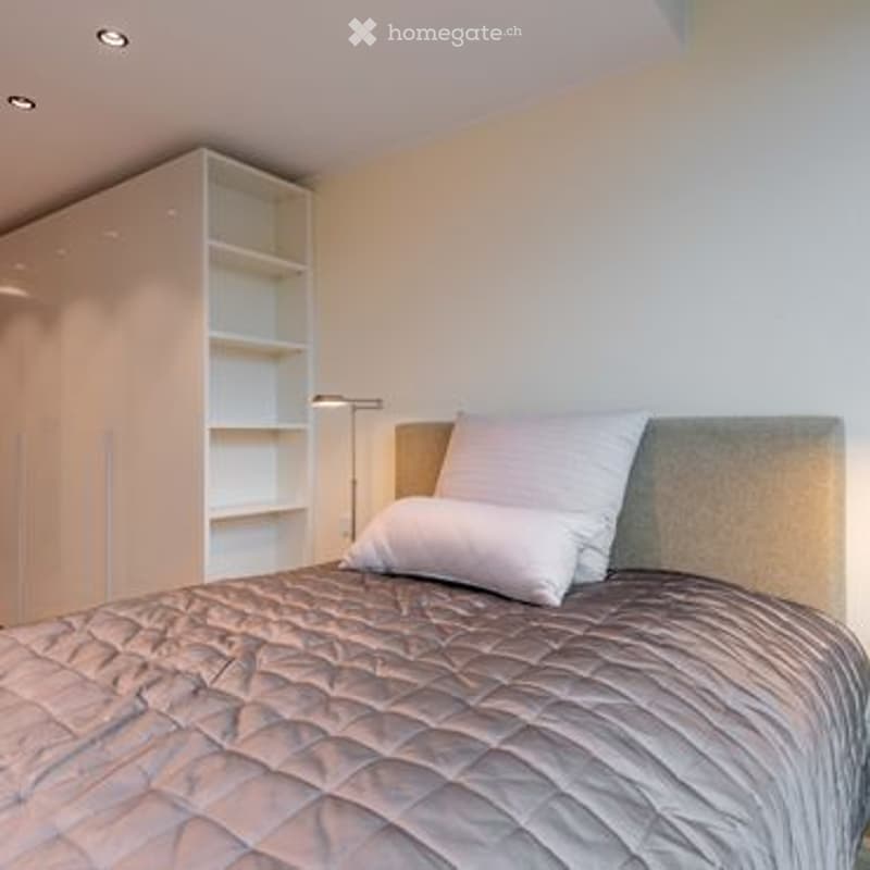 Modern bedroom with a grey headboard, white bedding, and a built-in wardrobe with shelves.