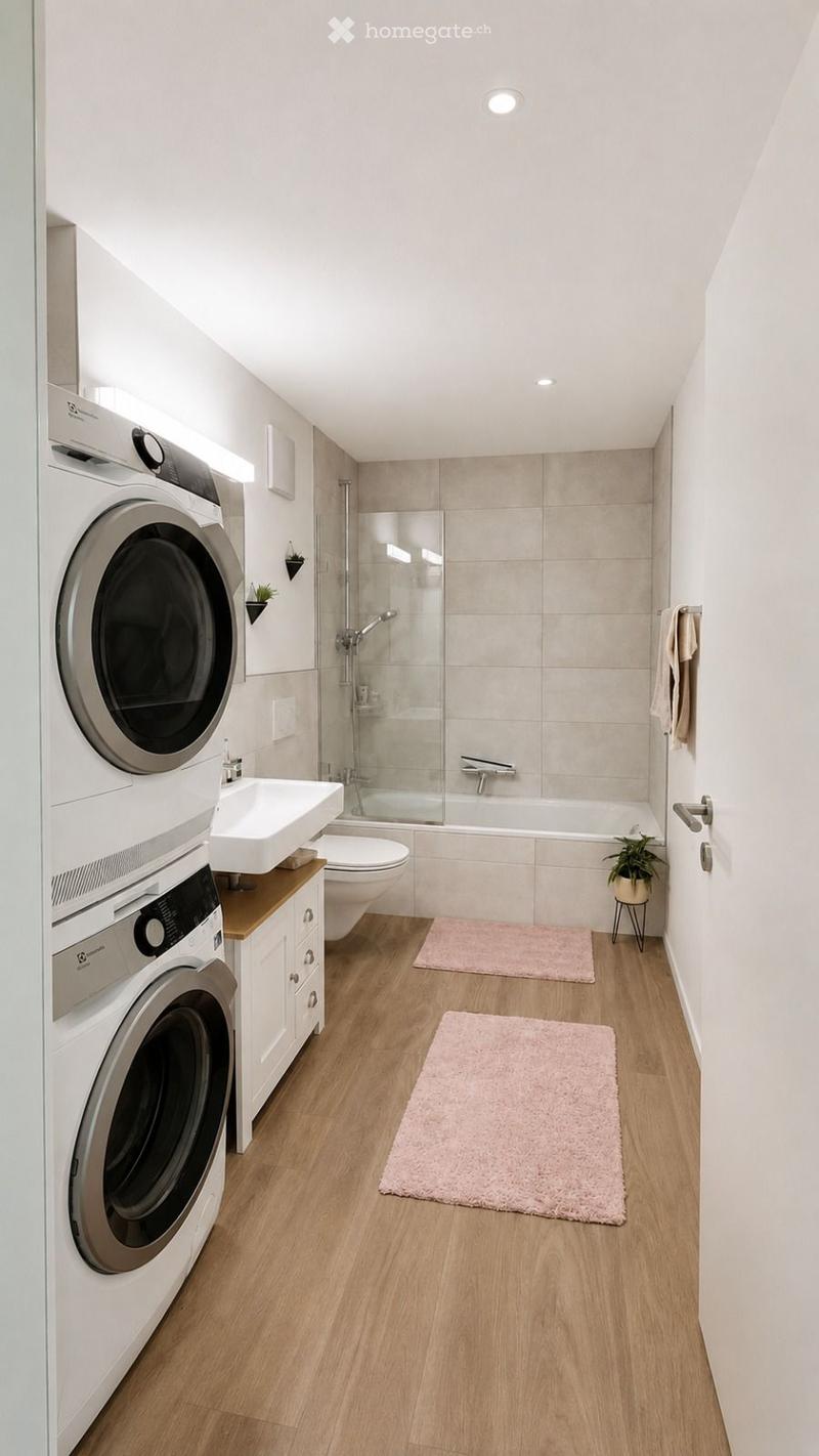 Modern bathroom with wooden flooring, white walls, a washing machine and dryer unit, a sink, toilet, bathtub with a glass shower enclosure, and two pink rugs.