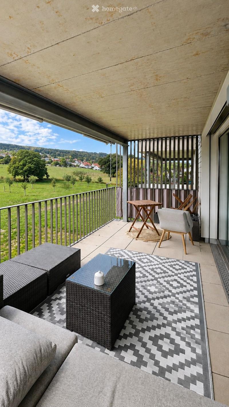 Balcony with modern furniture, including a sofa, coffee table, and chairs, overlooking a scenic countryside view.