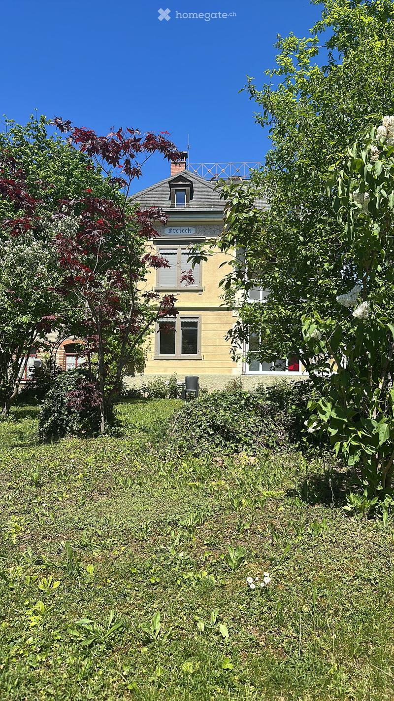 Two-story house with yellow siding, white trim, and multiple windows, surrounded by trees and greenery.
