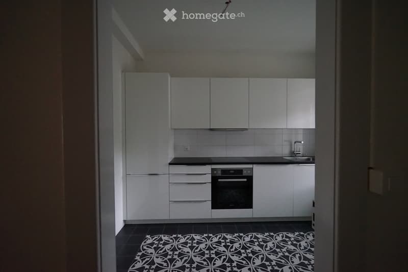 Modern kitchen with white cabinets, black countertop, built-in oven, and a decorative black and white tile floor.