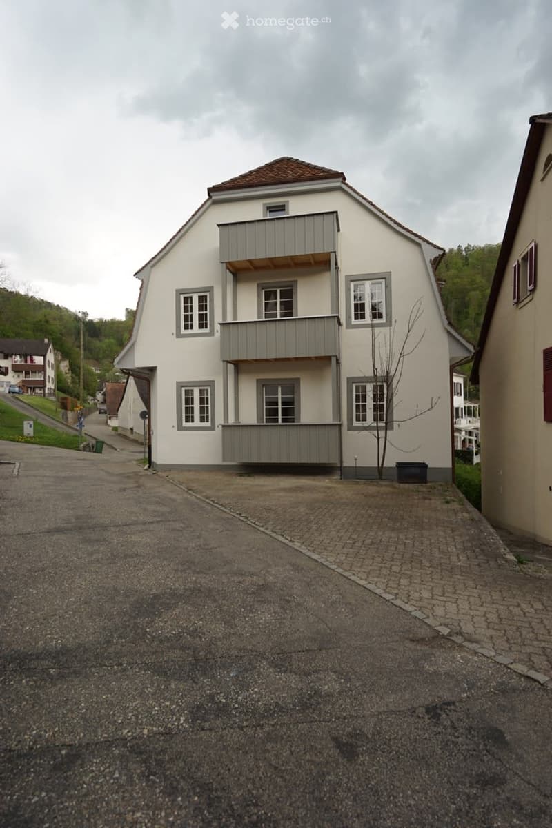 Two-story house with white exterior, grey trim, multiple windows, and a balcony on the upper floor.