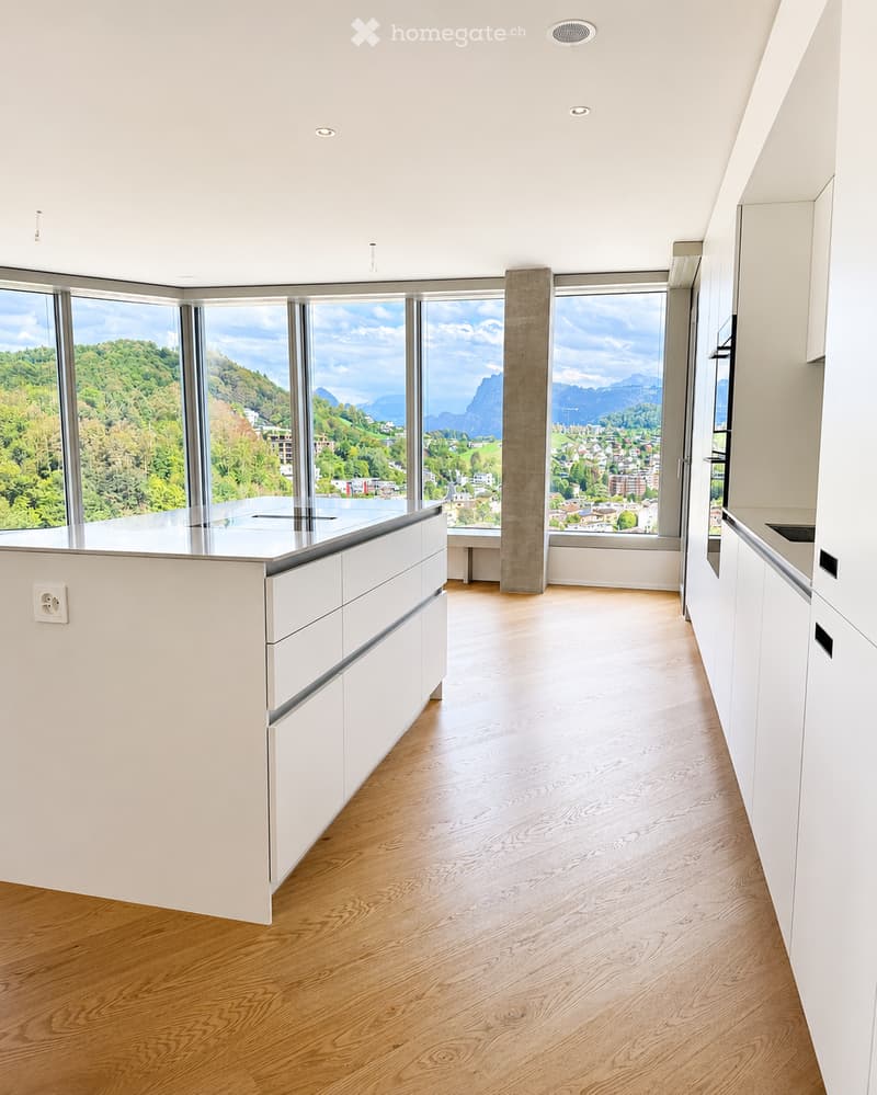 Modern, minimalist kitchen with white cabinets, a central island, and large windows offering a scenic mountain view.