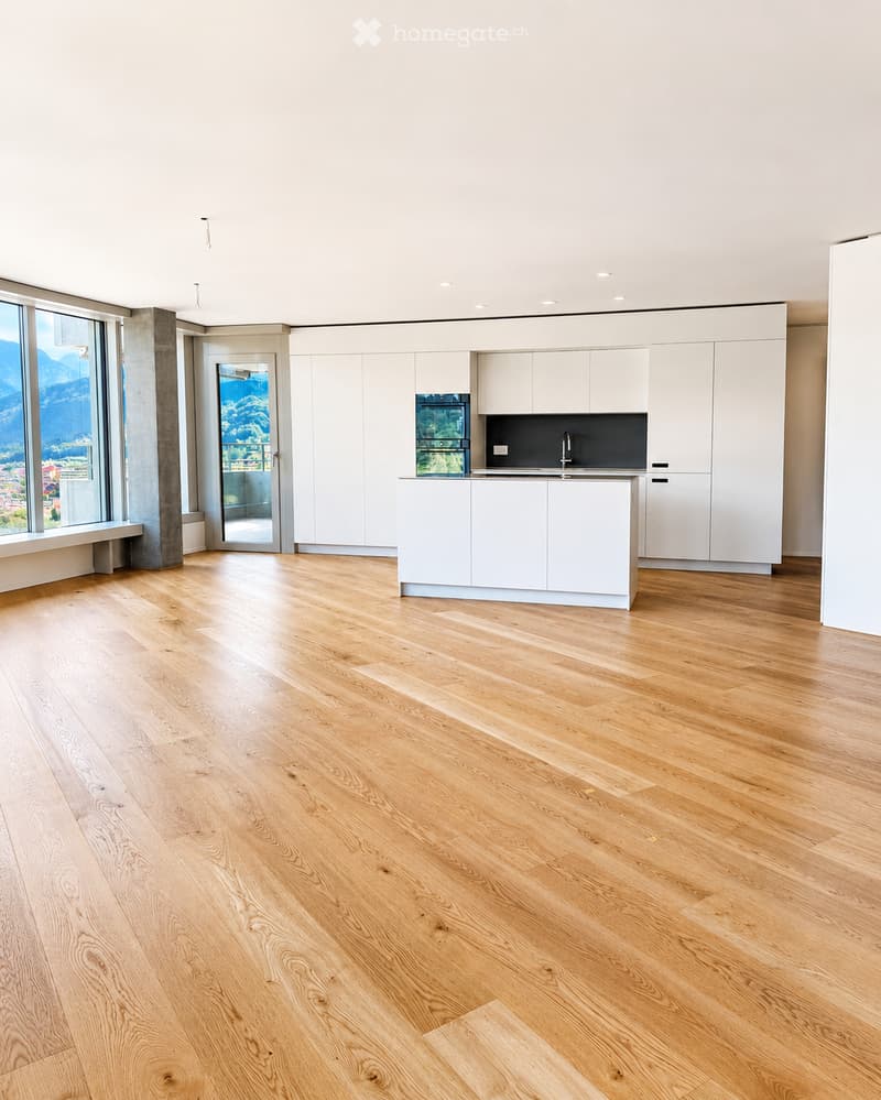 Empty kitchen with white cabinets, wooden flooring, and large windows offering a scenic view.