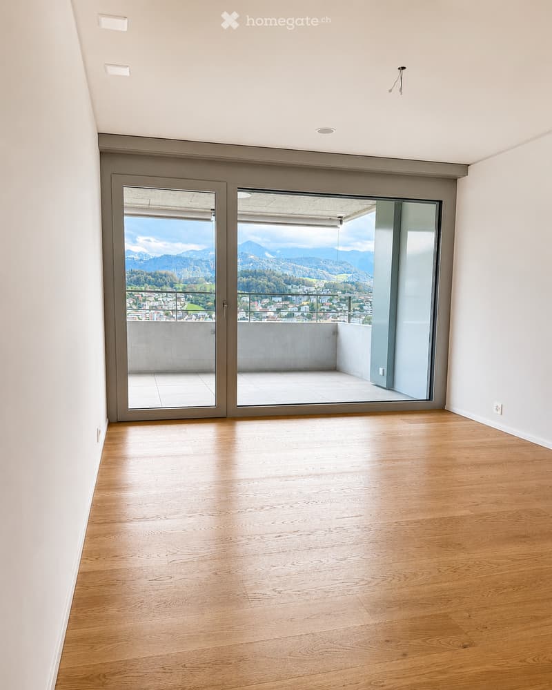 Empty room with wooden flooring, white walls, and large sliding glass doors leading to a balcony with a scenic mountain view.