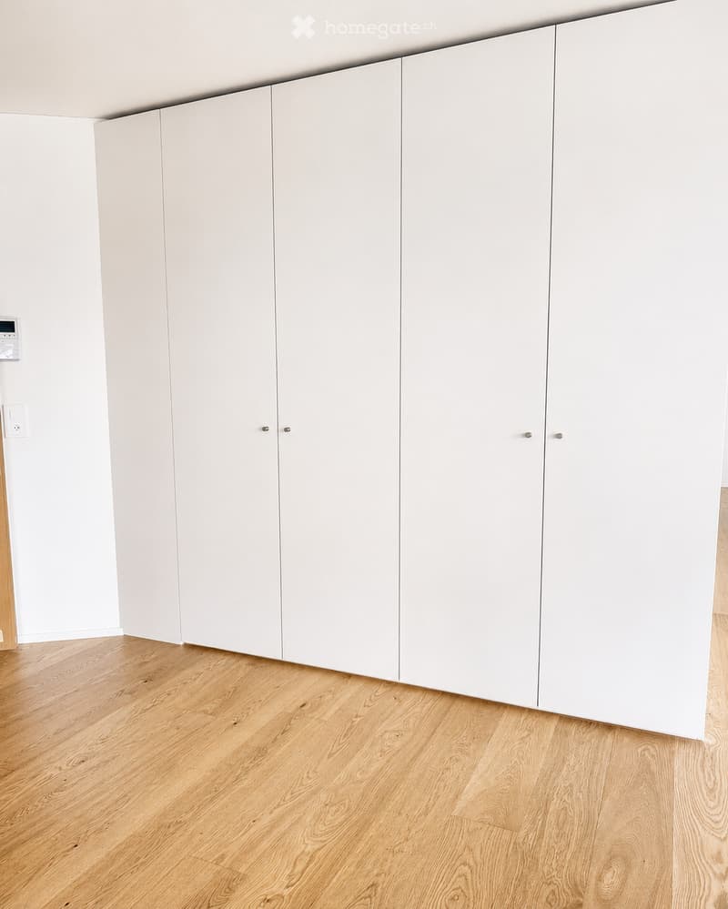 Empty room with light wooden flooring and white built-in wardrobes along one wall.