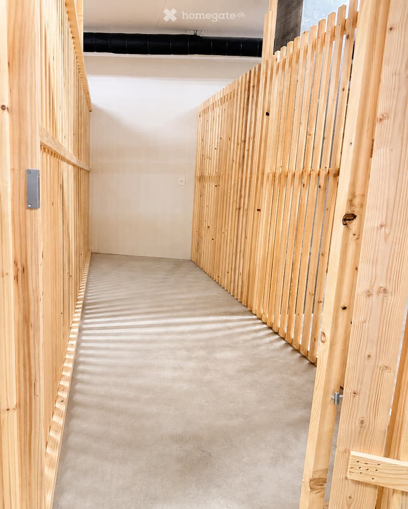 Empty hallway with wooden paneling on both sides and a concrete floor, featuring a black duct running along the ceiling.
