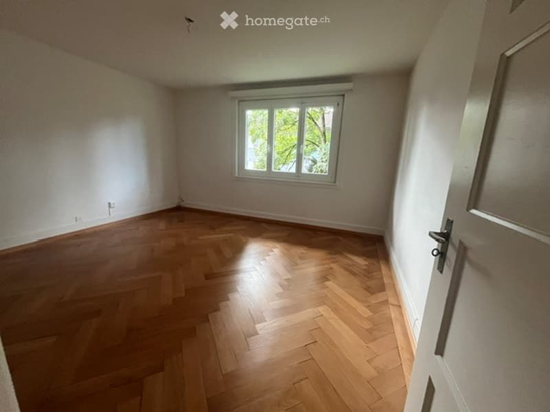 Empty room with wooden parquet flooring, white walls, and a single window letting in natural light. No furniture or equipment present.