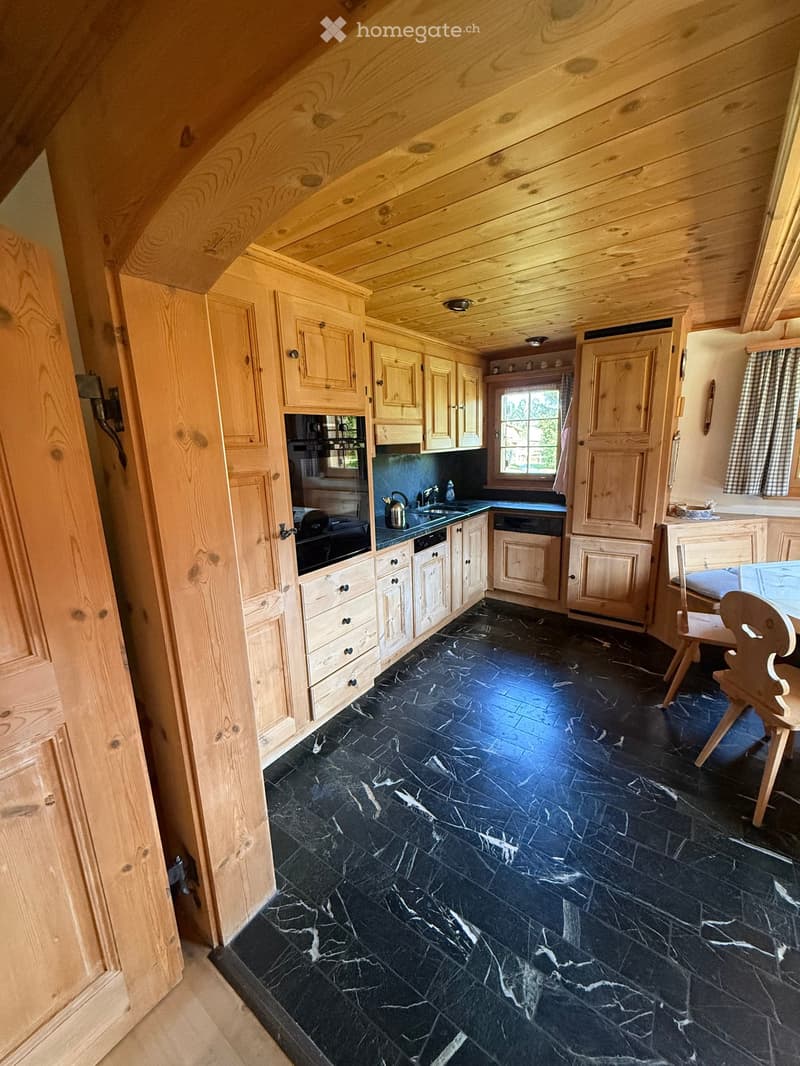 Kitchen with wooden cabinets, black marble flooring, sink, oven, dishwasher, and a small dining area with a table and chairs.