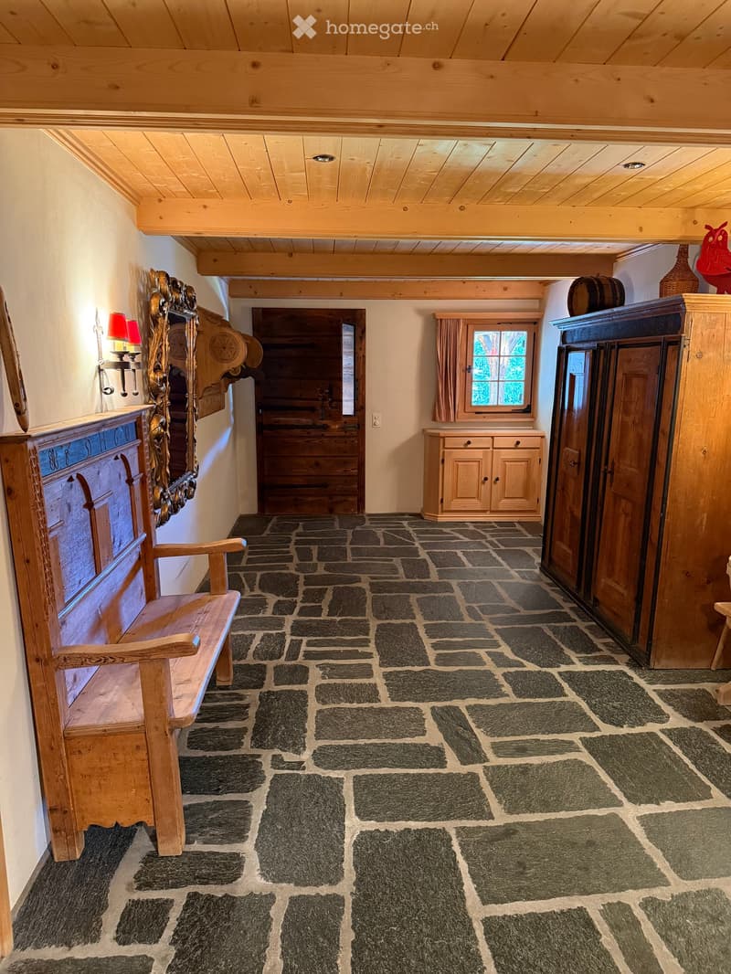 Cozy hallway with exposed wooden beams, stone-tiled floor, wooden bench, and built-in cabinets.