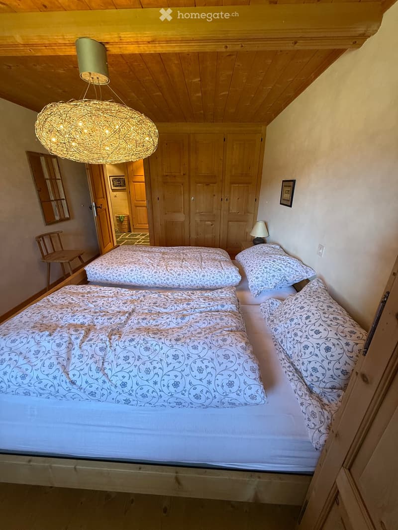 Cozy bedroom with two single beds, wooden wardrobe, a small chair, and a decorative hanging light fixture.