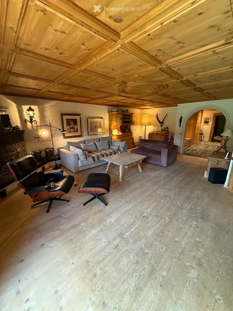 Living room with wooden floors, exposed wooden ceiling beams, a fireplace, a sofa, coffee table, chairs, and lamps.
