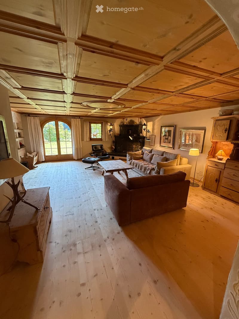 Spacious living room with wooden floors, exposed wooden ceiling beams, large windows, fireplace, sofa, coffee table, armchairs, and lamps.