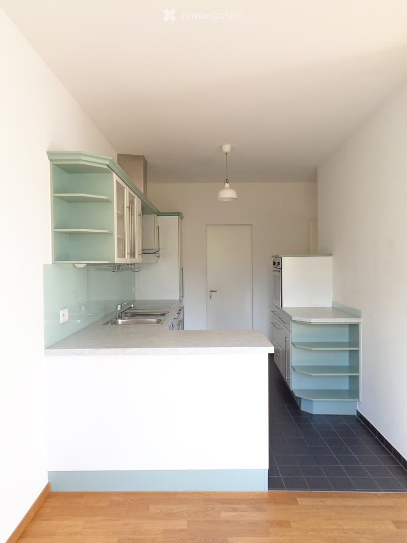 Modern kitchen with light blue cabinets, white countertops, and a central island. Features a sink, oven, refrigerator, and pendant light.