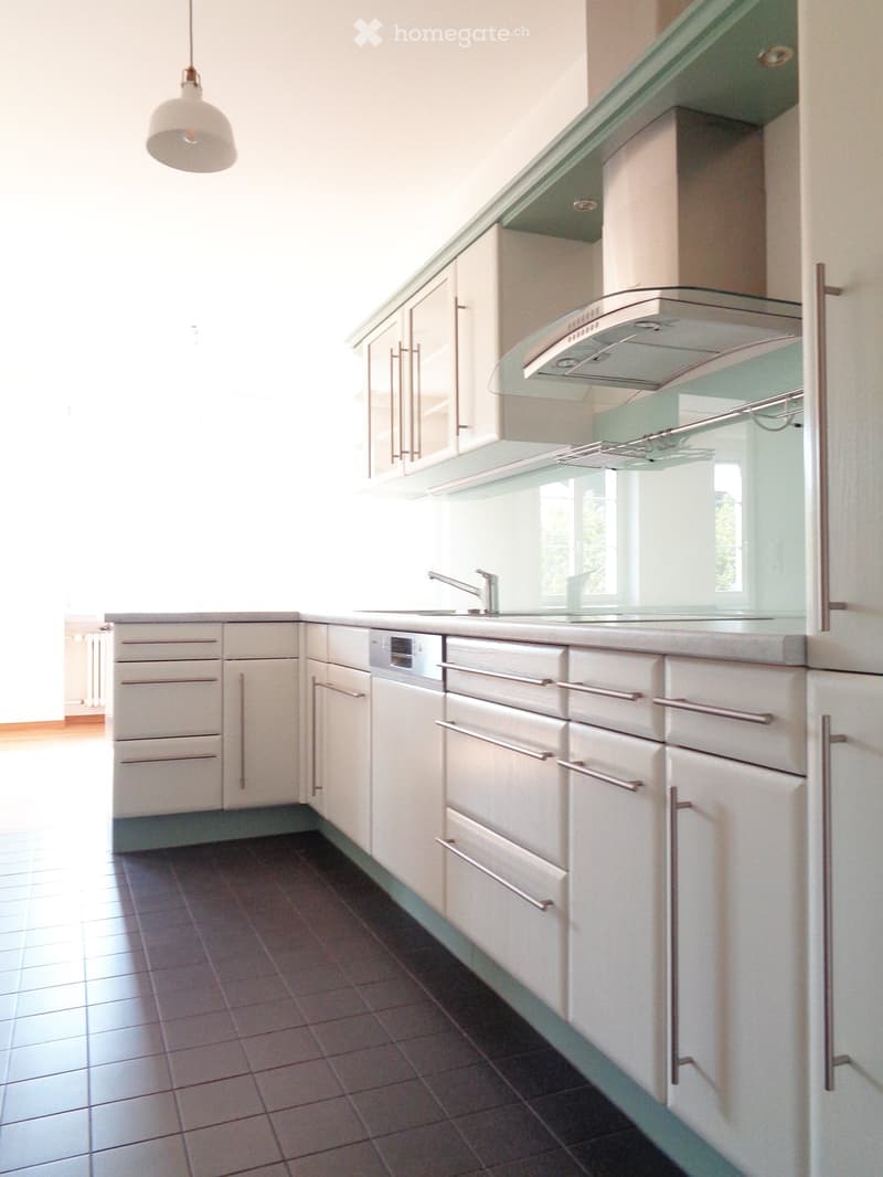 Modern kitchen with white cabinets, stainless steel appliances, and a dark tiled floor.