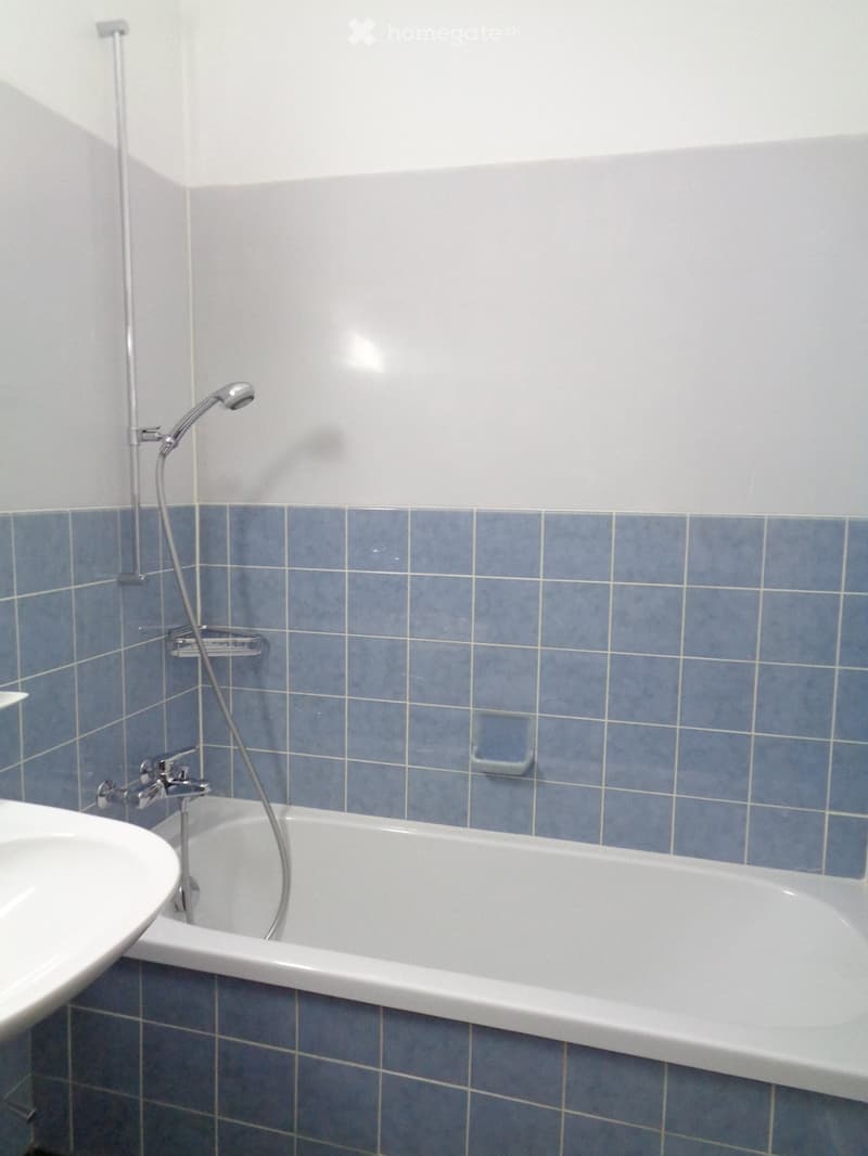 Bathroom with a bathtub, showerhead, faucet, and sink. Blue tiled walls and white fixtures.