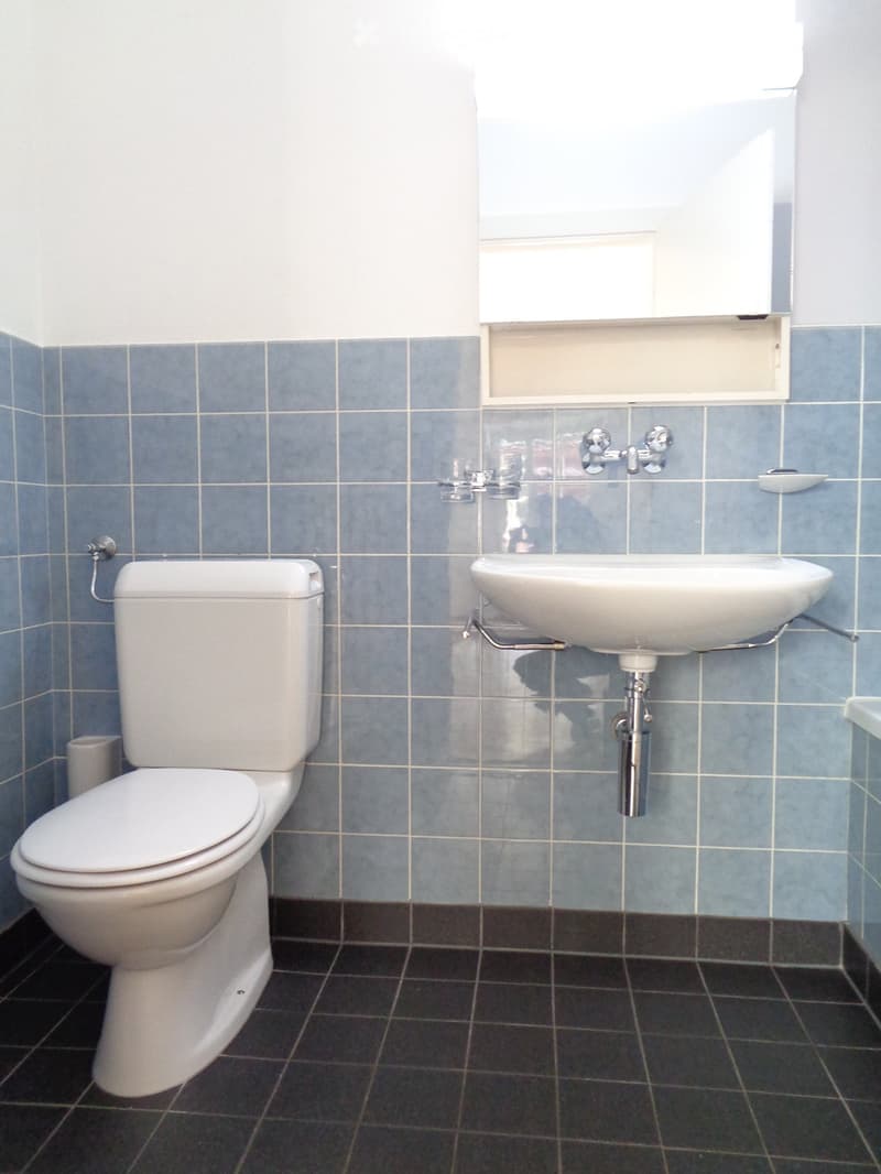 Bathroom with blue tiled walls, white toilet, and white sink with chrome faucet.