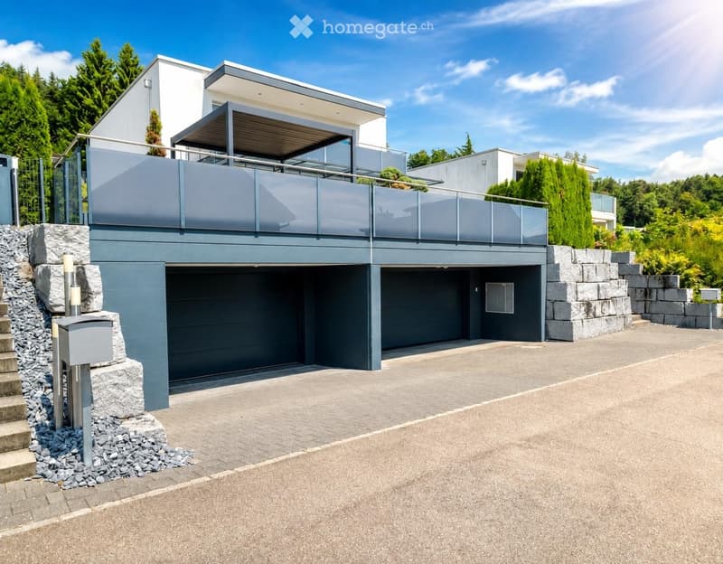 Modern two-story house with a grey garage, a raised balcony, and a stone staircase leading to the entrance.