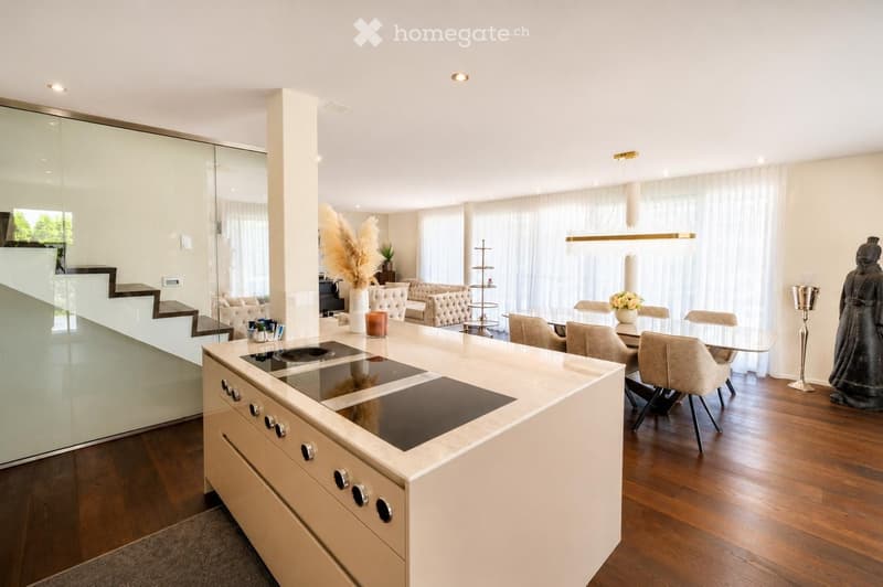 Modern kitchen with a white island, induction cooktop, and built-in cabinets. The space is open to a living area with a sofa, dining table, and chairs. Decorative elements include a vase with dried plants, a candle, and a statue.