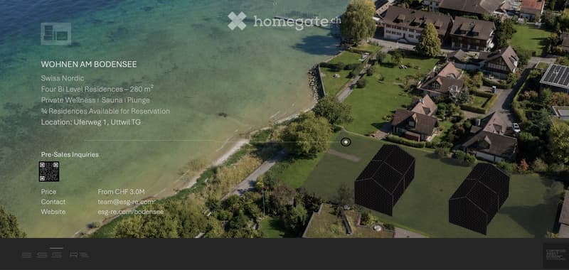 Aerial view of a residential area near a lake, featuring multiple houses, green lawns, and a waterfront with a pier extending into the water.