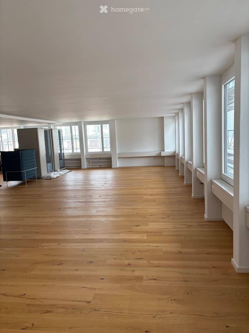 Empty room with wooden flooring, white walls, large windows, and radiators. No furniture or equipment present.