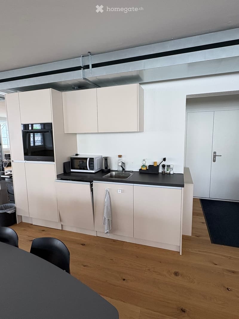 Modern kitchen with light-colored cabinets, black countertop, microwave, coffee maker, sink, and a small table with chairs.