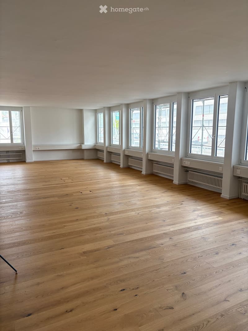 Empty room with wooden flooring, large windows, and radiators along the walls.