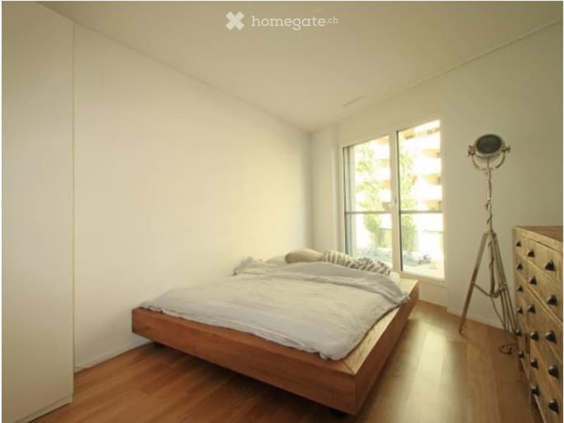 Minimalist bedroom with a wooden bed, nightstand, and a floor lamp near a large window.