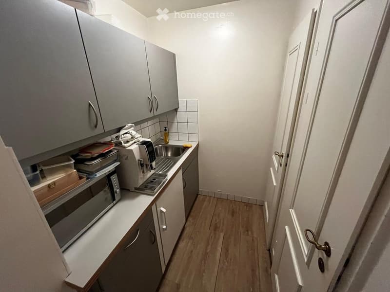 Modern kitchen with grey cabinets, white tiled backsplash, wooden flooring, and stainless steel appliances including a microwave, oven, and toaster.