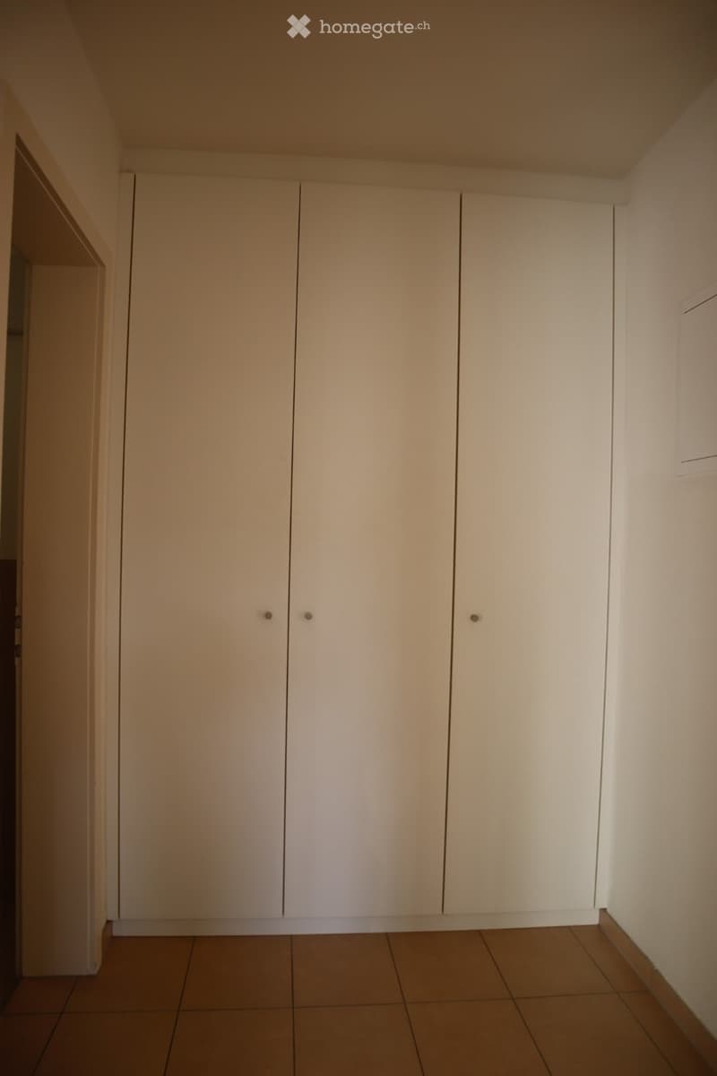 Empty room with beige tiled floor, white walls, and large built-in white closet with double doors.