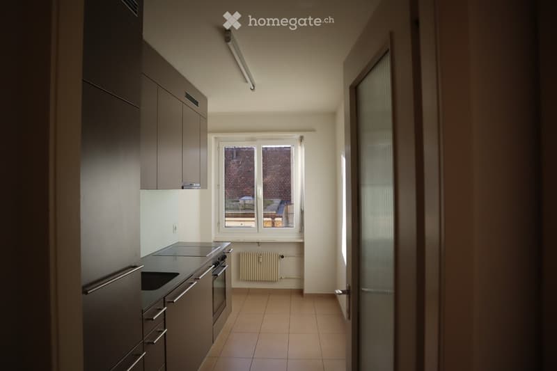 Modern kitchen with dark cabinets, stainless steel appliances, tiled floor, and a window overlooking a courtyard.