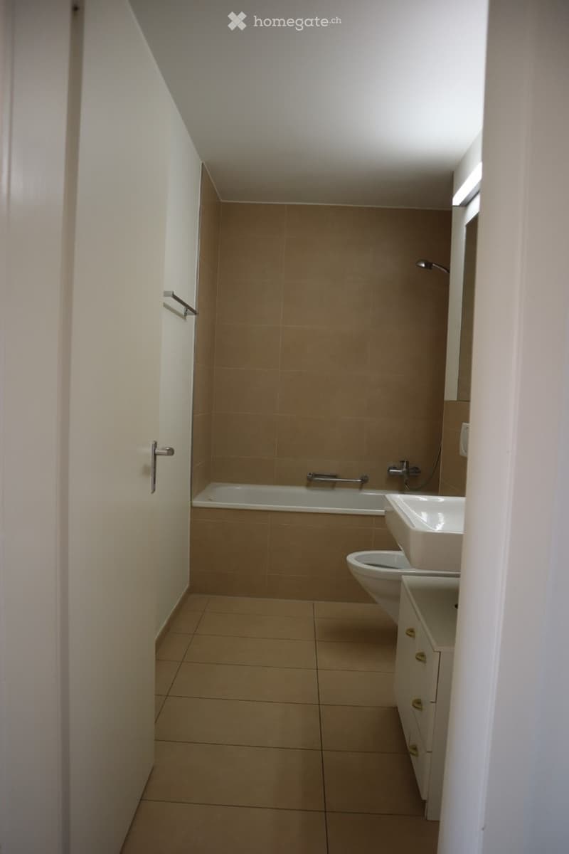 Modern bathroom with beige tiles, a bathtub, toilet, sink, and a showerhead.
