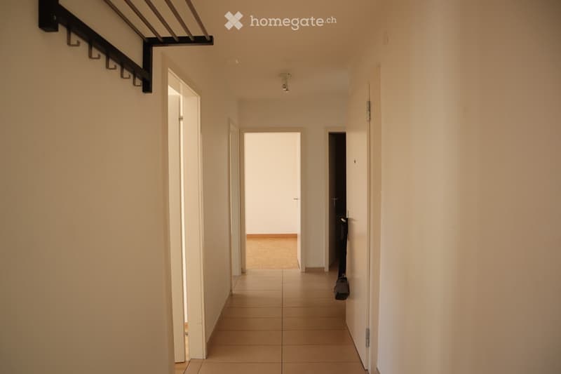 Empty hallway with tiled floor, white walls, and several doors leading to different rooms.