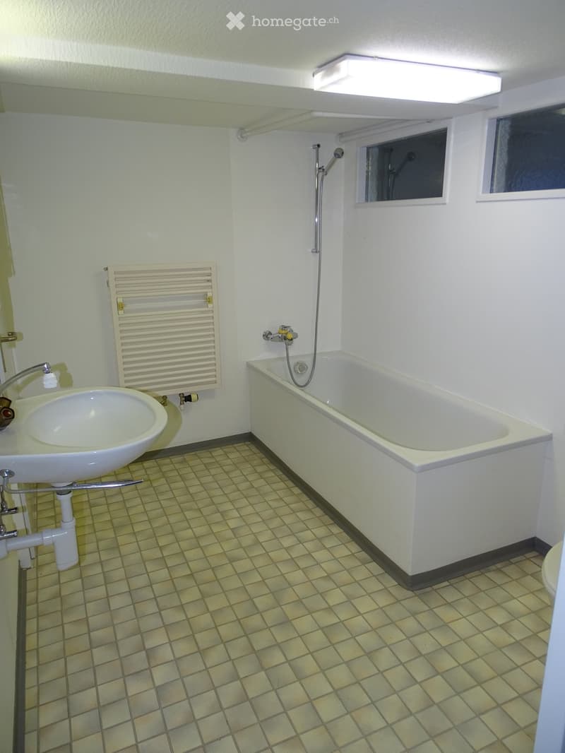 Bathroom with a bathtub, sink, faucet, and radiator. The room has tiled flooring and white walls.