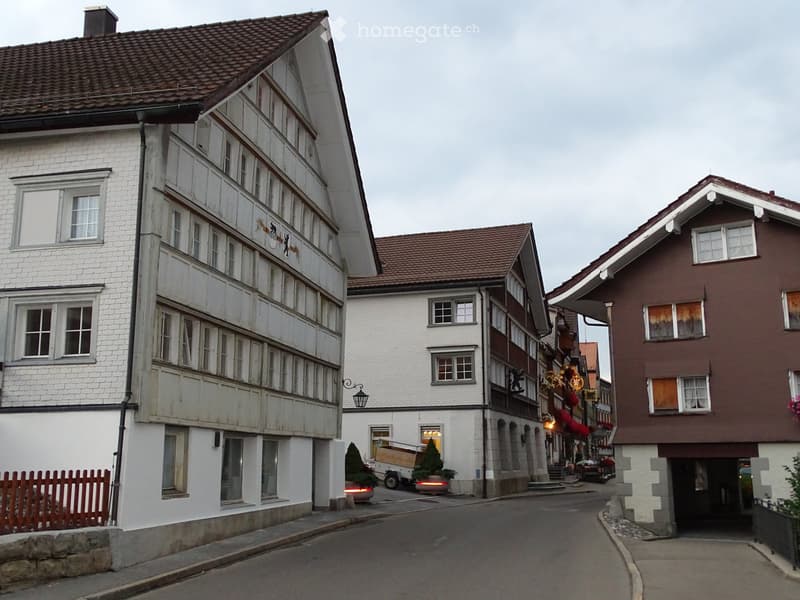 A row of traditional European buildings with white and brown facades, multiple windows, and decorative elements, situated along a narrow street.