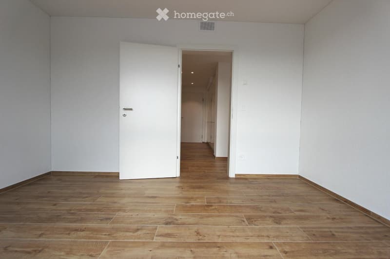 Empty room with wooden flooring and white walls, featuring an open doorway leading to another area.