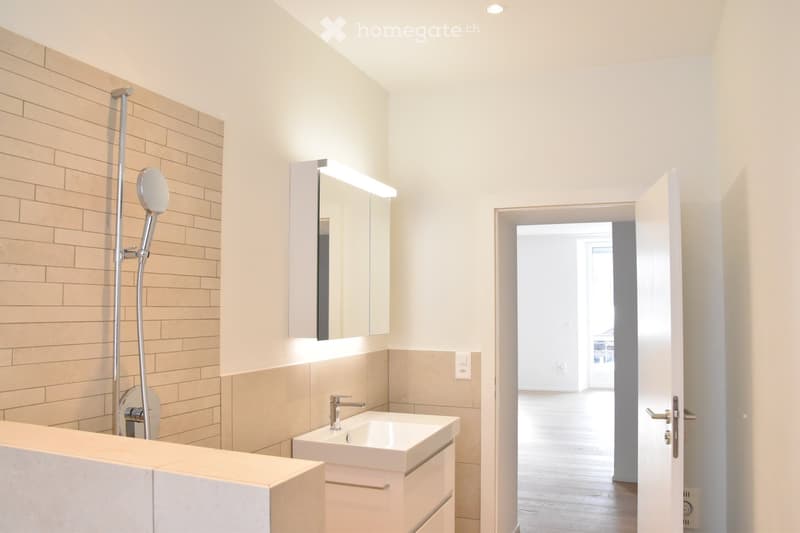 Bathroom with white sink, mirror, shower, and tiled walls