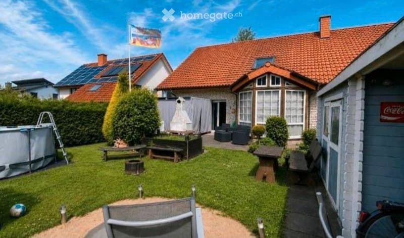 Well-maintained garden with a swimming pool, benches, a fire pit, and outdoor seating. Solar panels on the roof of the adjacent house.
