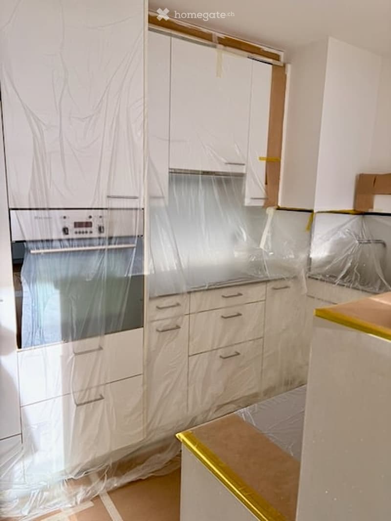 Kitchen with white cabinets, an oven, and protective plastic sheeting covering surfaces, indicating ongoing renovation or cleaning.