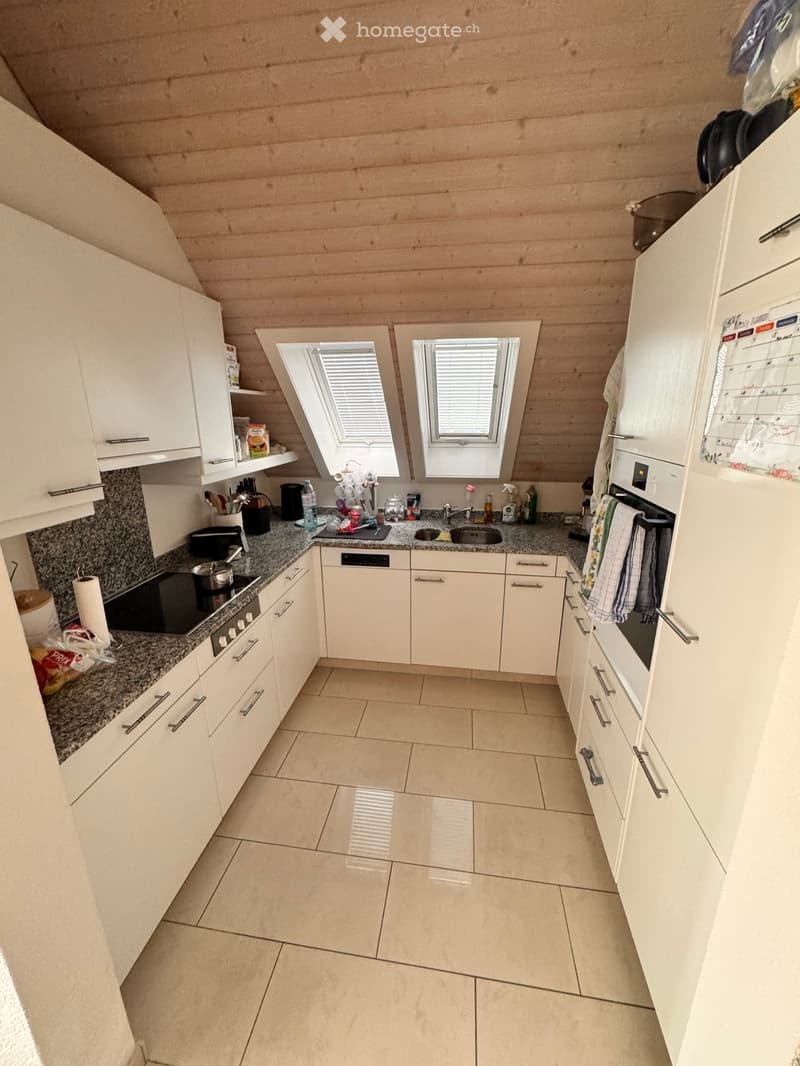 Modern kitchen with white cabinets, granite countertops, and stainless steel appliances. Features include a sink, oven, microwave, and refrigerator. The space has a clean, organized layout with tiled flooring and wooden ceiling beams.