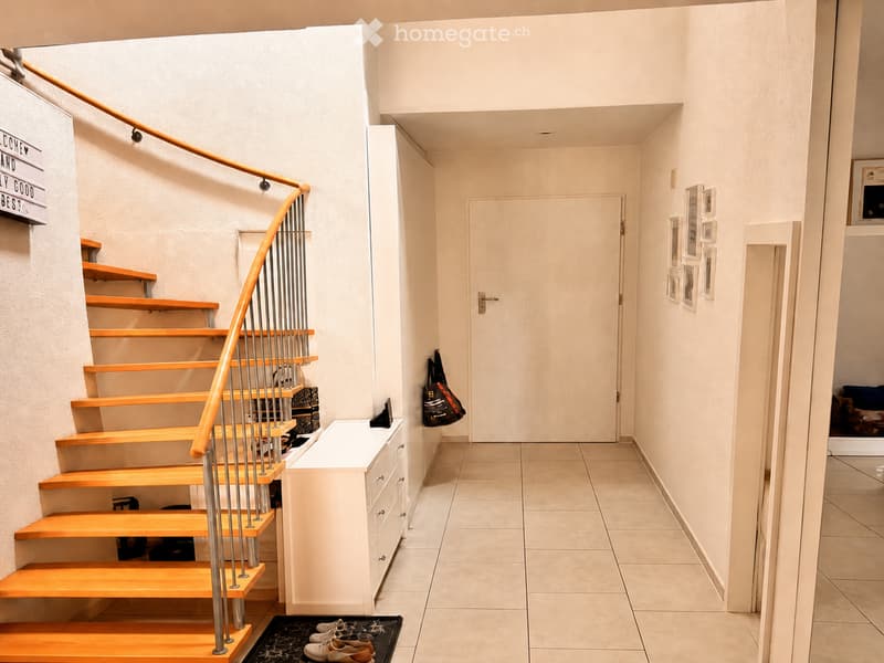 Hallway with tiled floor, wooden staircase with metal railing, white cabinet, and a door leading to another room.