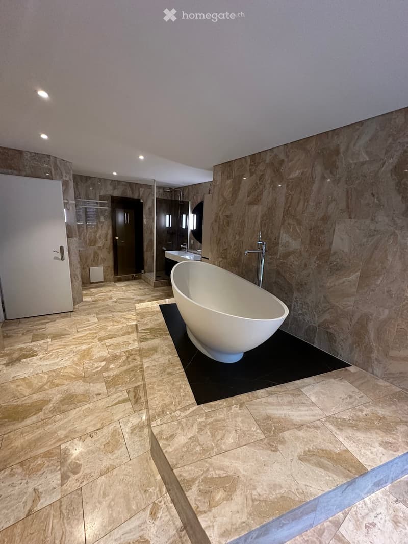 Spacious bathroom with a freestanding bathtub, stone tile walls and floors, and a modern vanity area.