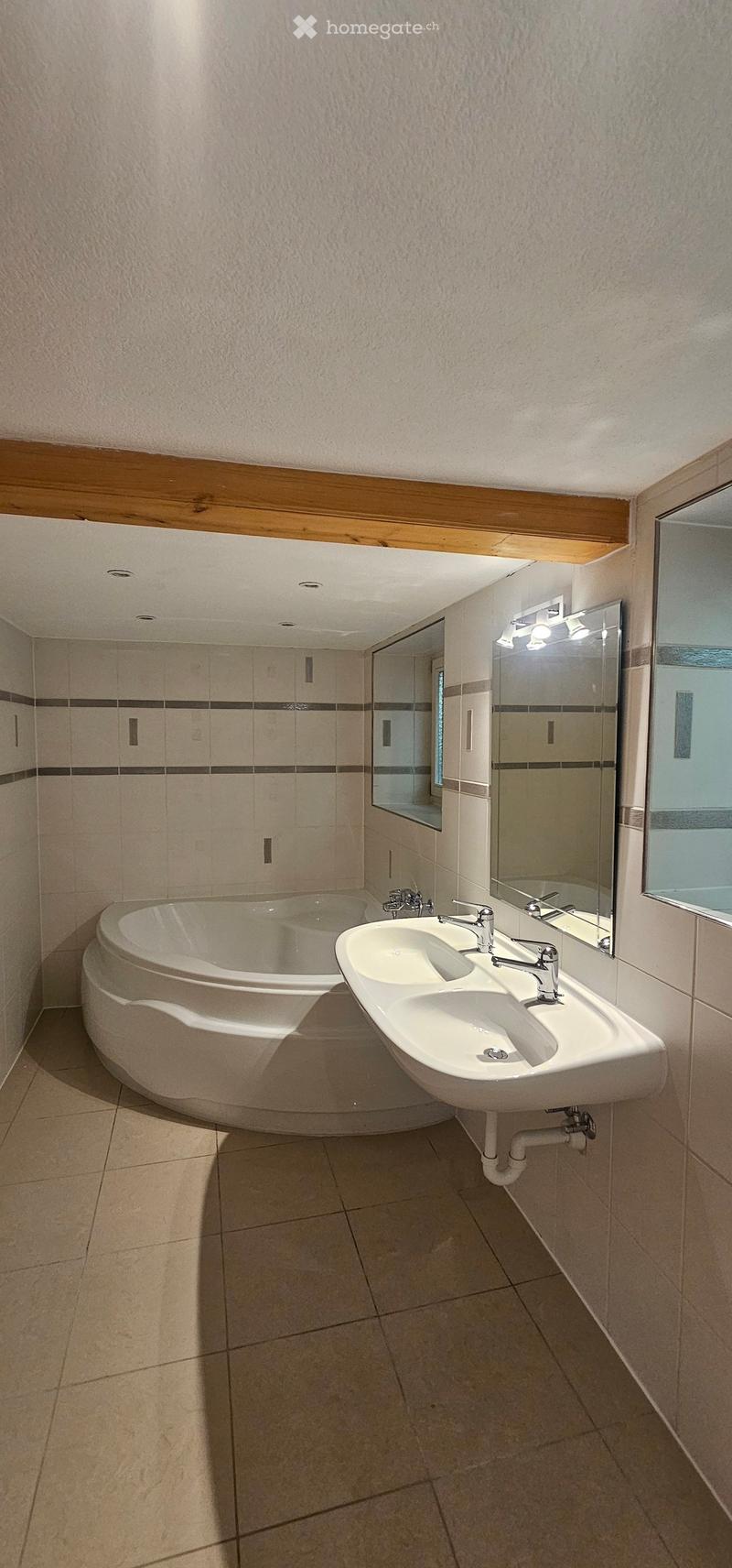 Modern bathroom with a curved bathtub, double sink, and large mirror. Light-colored tiles and wooden trim.