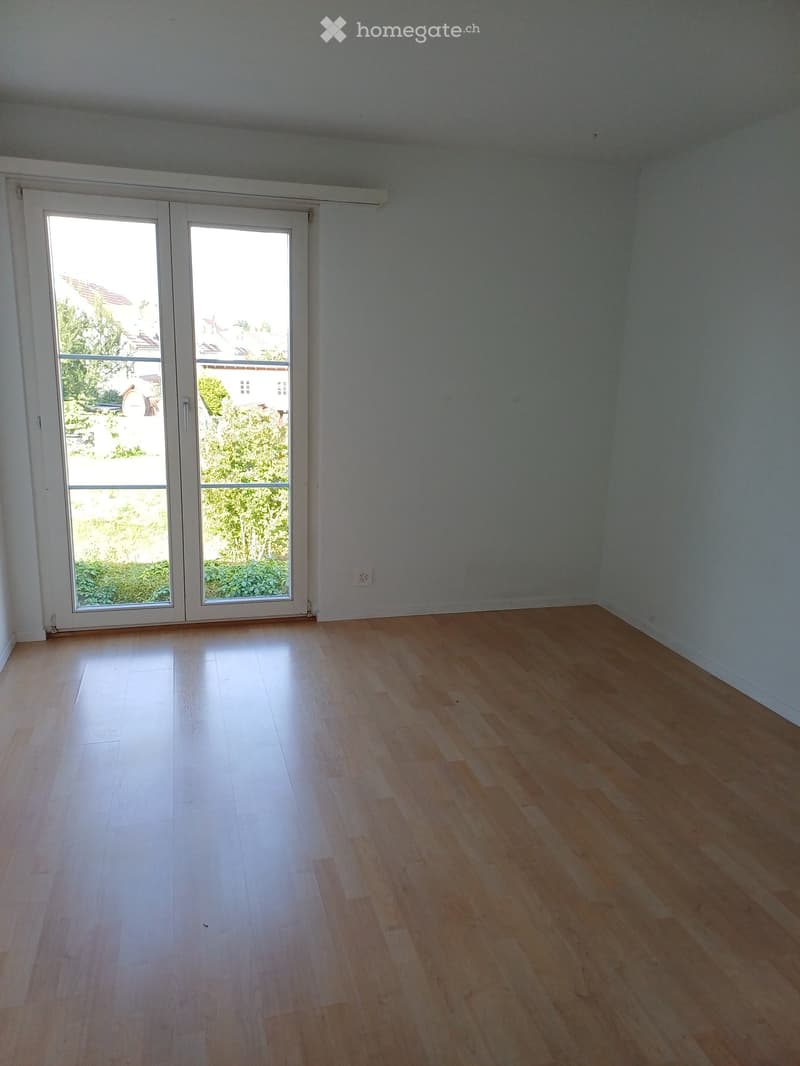 Empty room with light wooden flooring and white walls, featuring a large sliding glass door leading to an outdoor area.